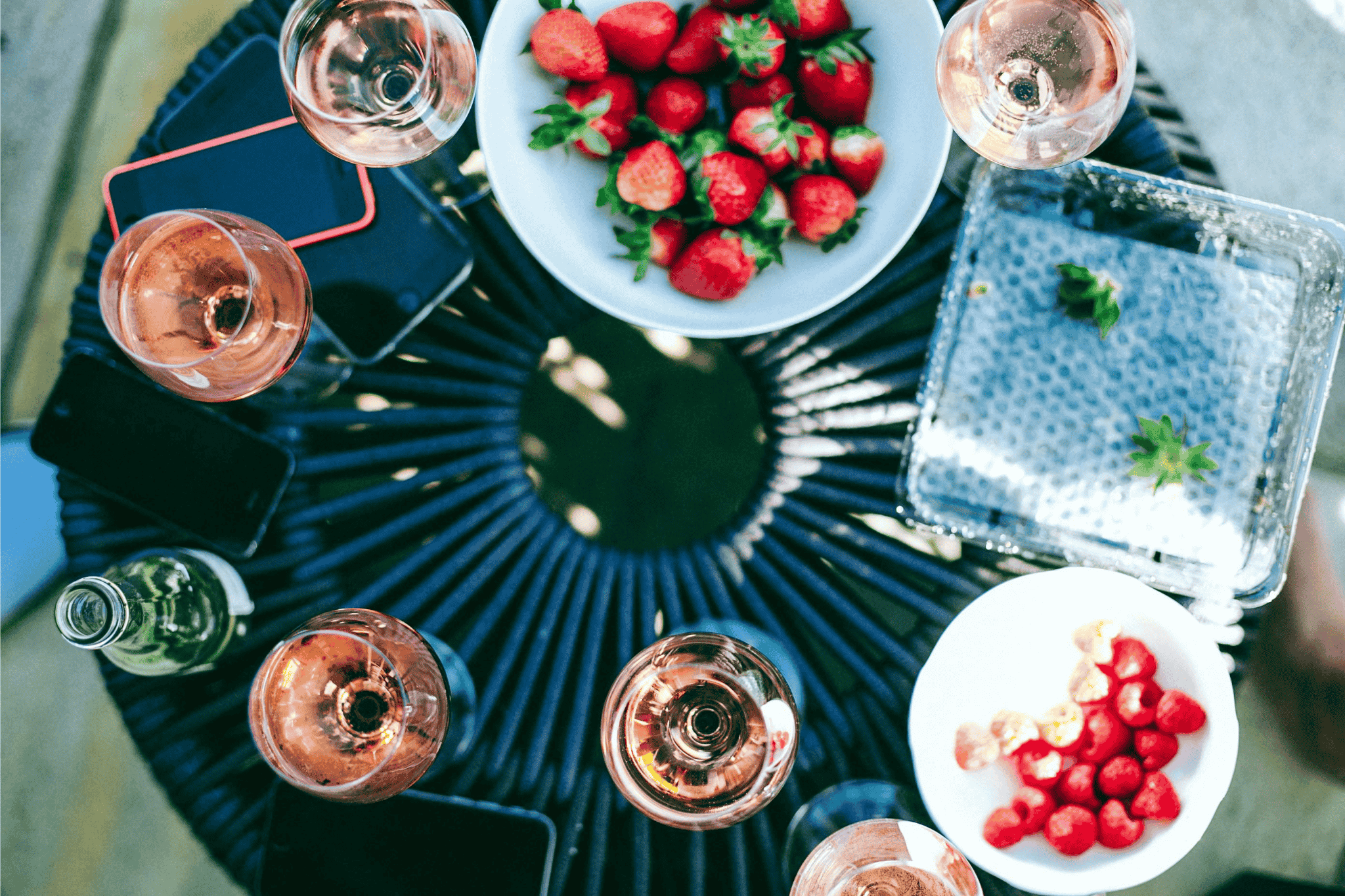 Glasses of ros wine on a table surrounded by fresh strawberries and friends' phones during a casual outdoor gathering